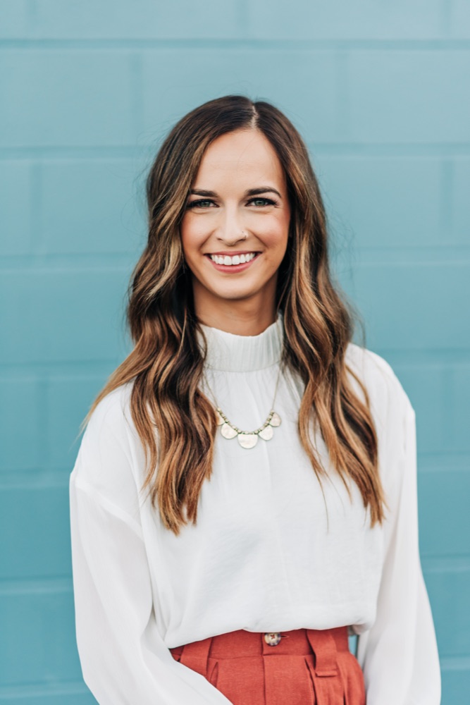 Portrait of Anna Quintero smiling, standing in front of a teal wall